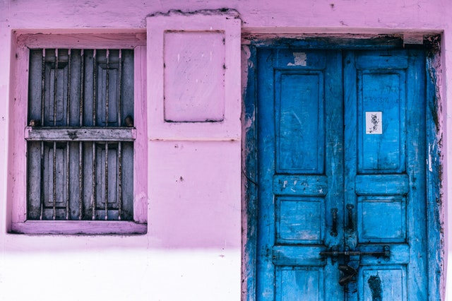 Modré drevené dvere vedľa ružovej steny a dreveného okna